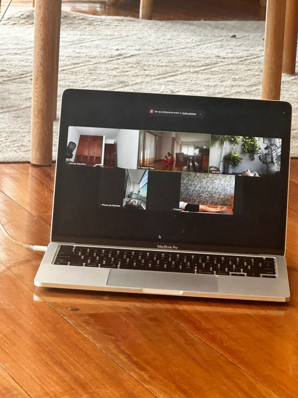 Laptop on a wooden floor showing a video call with multiple participants.